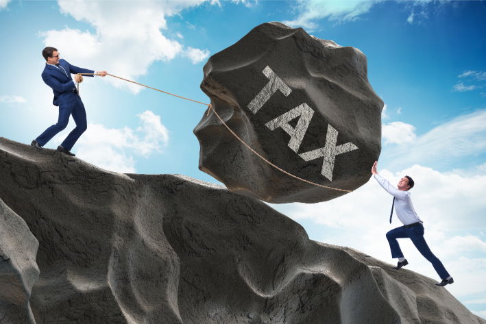 Two individuals are depicted on a cliff with one person at a higher elevation pulling a massive rock labeled "TAX" with a rope, while the other below pushes against it, symbolizing the challenging effort required to manage and overcome tax burdens associated with selling real estate in Ohio.