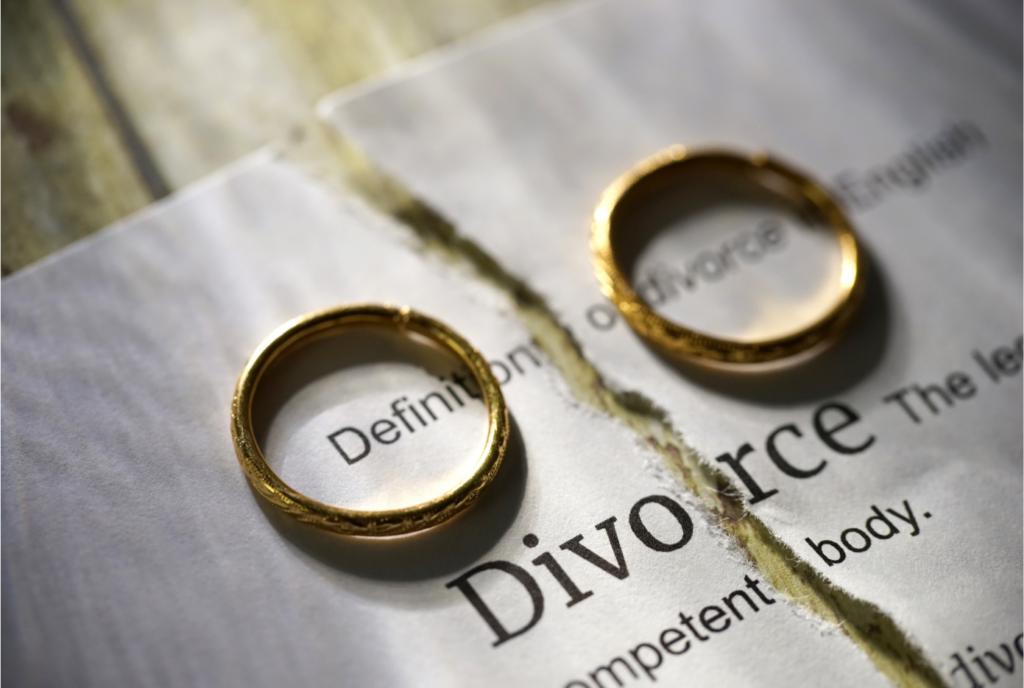 Two golden wedding rings on a torn piece of paper with the word "Divorce" visible, symbolizing the end of a marriage.