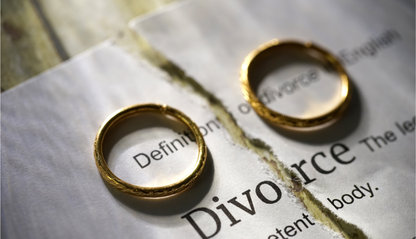 Two golden wedding rings on a torn piece of paper with the word "Divorce" visible, symbolizing the end of a marriage.