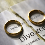 Two golden wedding rings on a torn piece of paper with the word "Divorce" visible, symbolizing the end of a marriage.