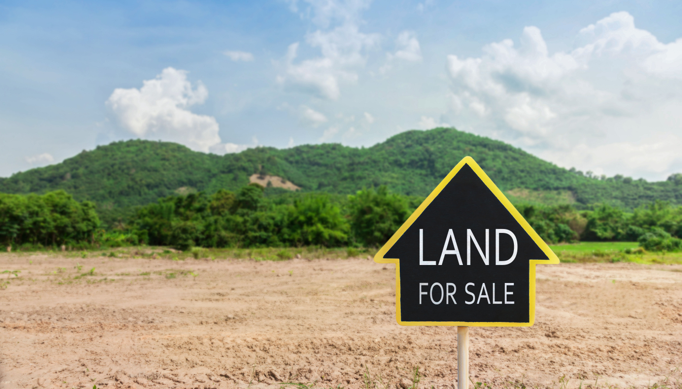 Yellow 'Land for Sale' sign on an empty lot with a lush green mountainous backdrop in Ohio, symbolizing private land sales opportunities.