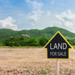 Yellow 'Land for Sale' sign on an empty lot with a lush green mountainous backdrop in Ohio, symbolizing private land sales opportunities.