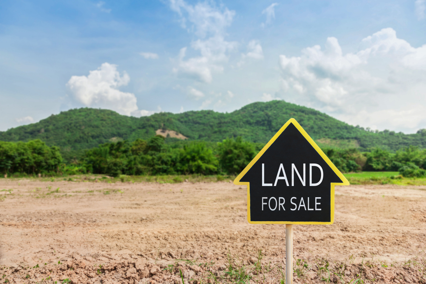 Yellow 'Land for Sale' sign on an empty lot with a lush green mountainous backdrop in Ohio, symbolizing private land sales opportunities.