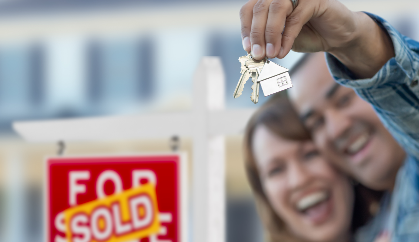 Happy couple with new house keys in front of sold sign in Ohio