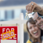 Happy couple with new house keys in front of sold sign in Ohio