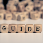 Wooden blocks spelling the word GUIDE on a white surface, symbolizing a comprehensive resource for home sellers on NAR commission settlement questions.