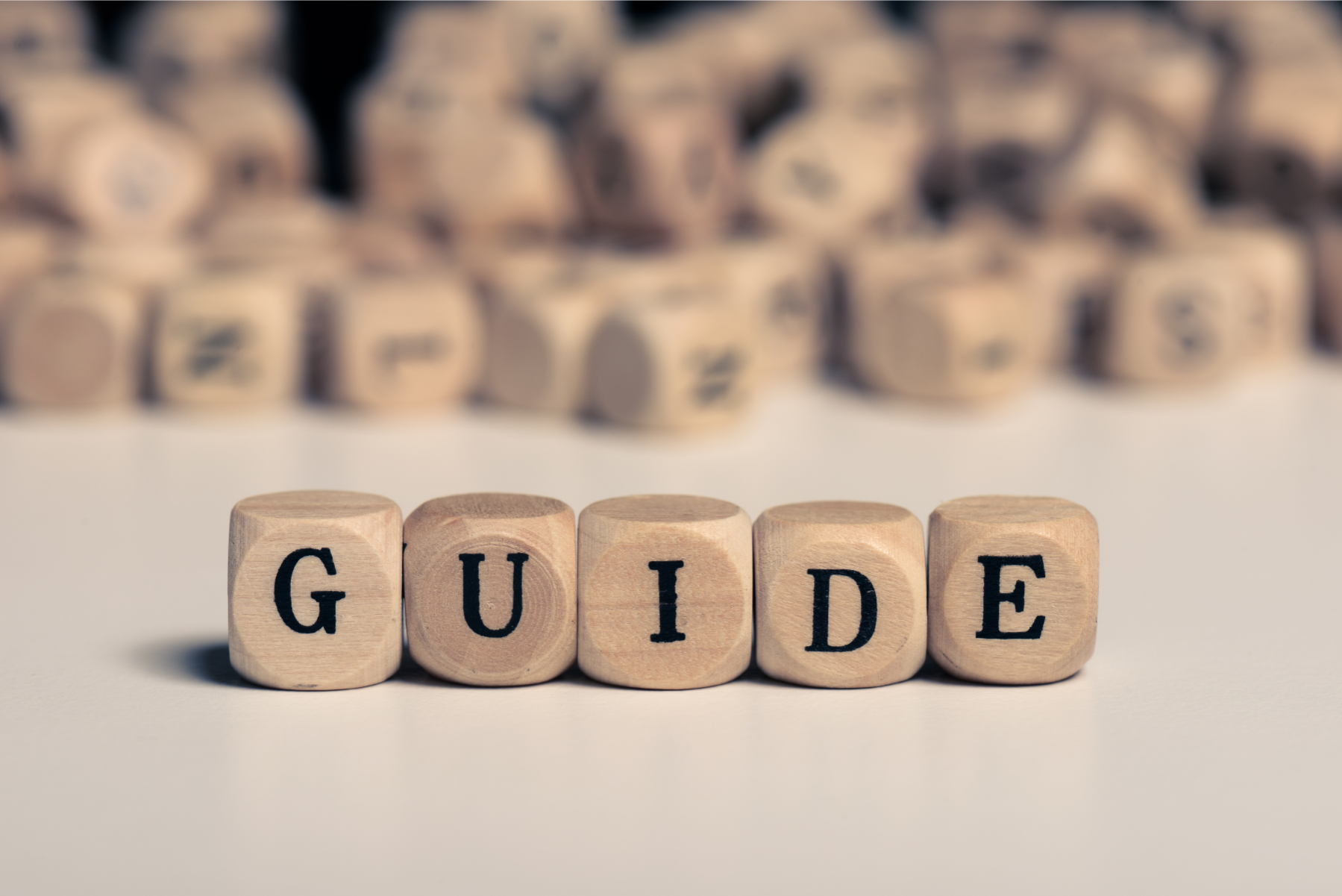 Wooden blocks spelling the word GUIDE on a white surface, symbolizing a comprehensive resource for home sellers on NAR commission settlement questions.