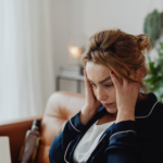 Stressed woman sitting on a couch at home with her head in her hands, looking worried, possibly contemplating missed mortgage payments in Ohio.
