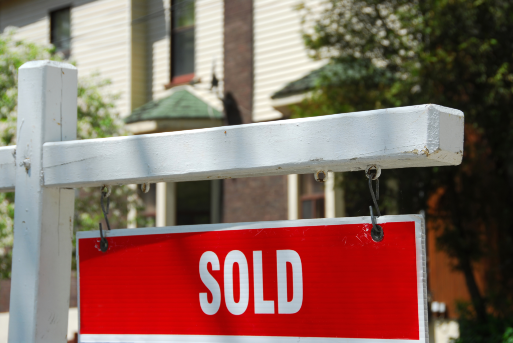 Close-up of a red 'SOLD' sign on a white post in front of a Dayton, Ohio house, symbolizing a fast home sale in the local real estate market.