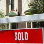 Close-up of a red 'SOLD' sign on a white post in front of a Dayton, Ohio house, symbolizing a fast home sale in the local real estate market.