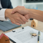 Real estate handshake over contract with house keys and wooden model home, symbolizing successful apartment building sale in Ohio.