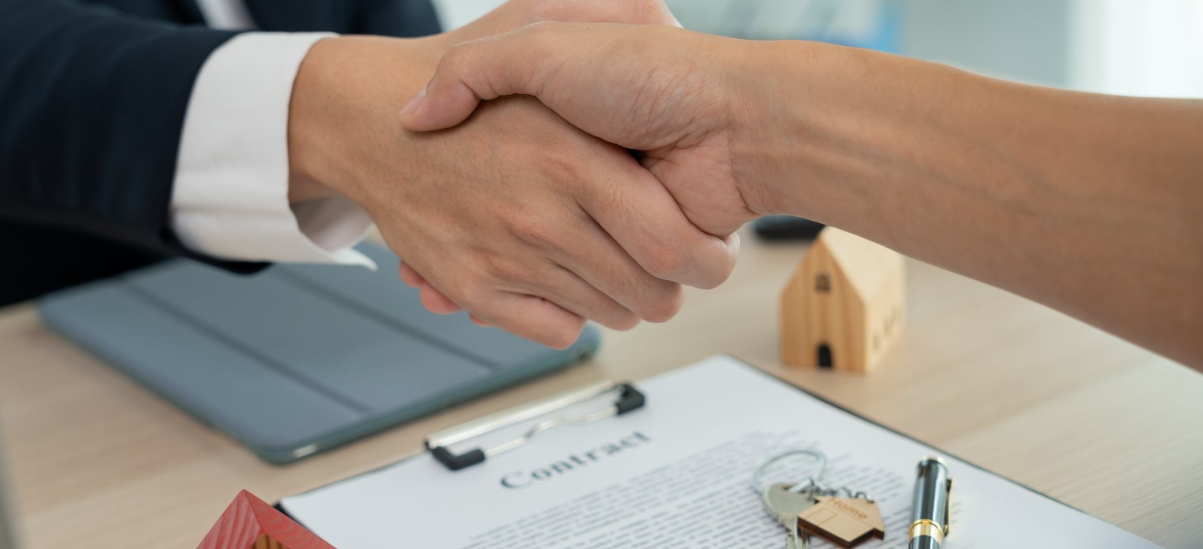 Real estate handshake over contract with house keys and wooden model home, symbolizing successful apartment building sale in Ohio.