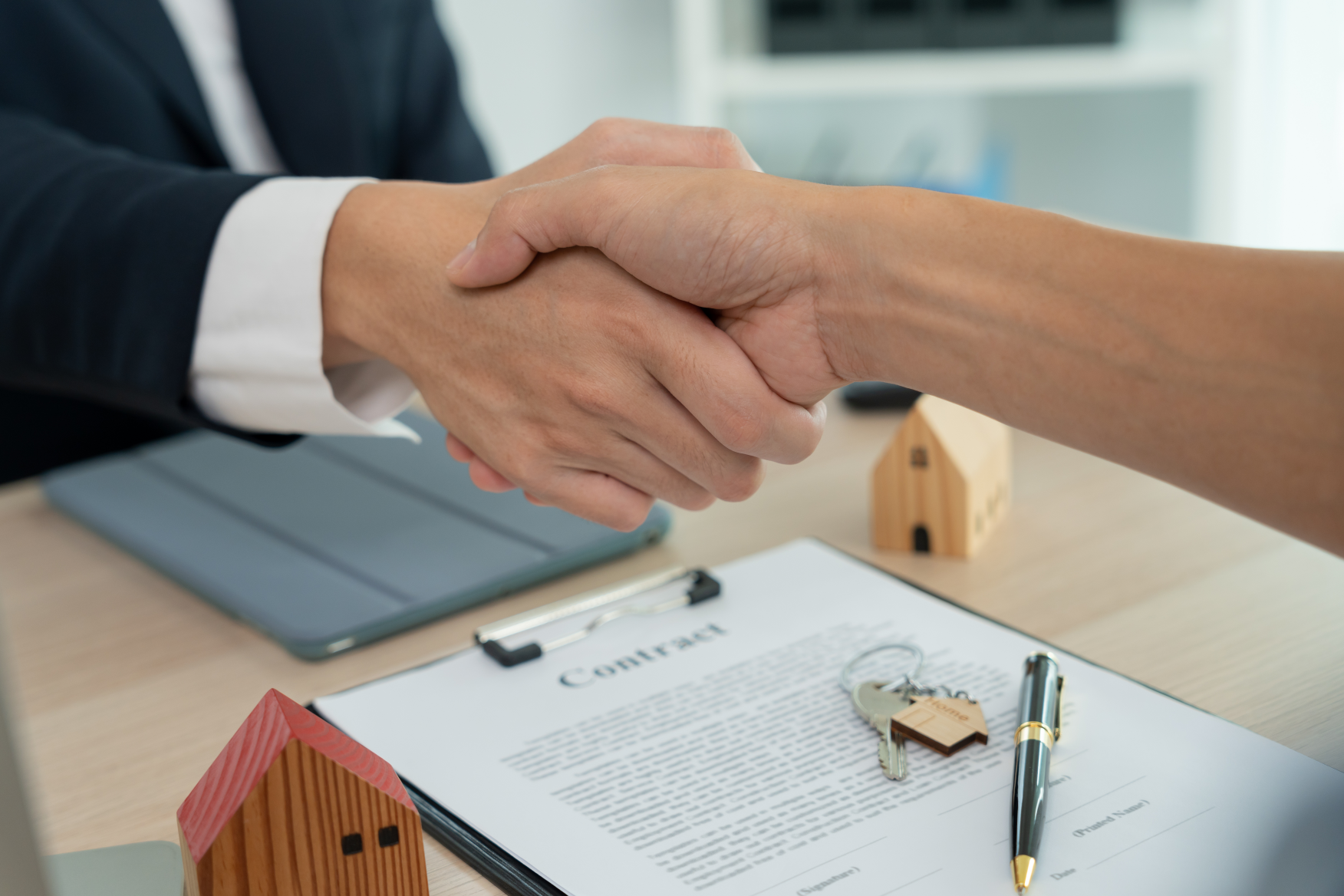 Real estate handshake over contract with house keys and wooden model home, symbolizing successful apartment building sale in Ohio.