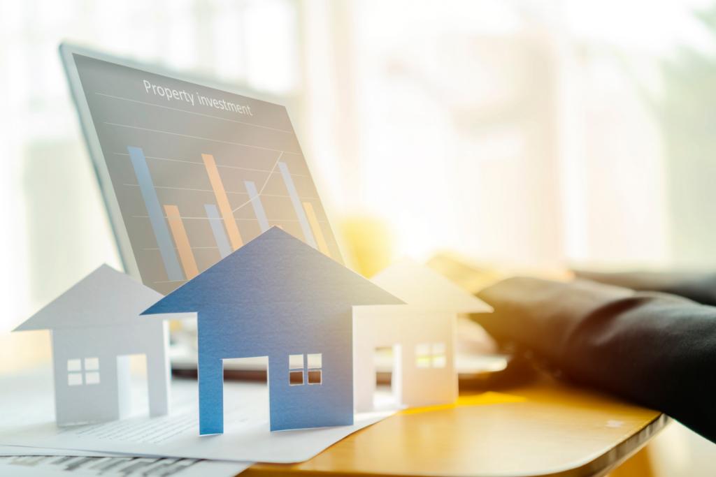 Paper cutouts of houses on a desk with laptop showing property investment charts, symbolizing Ohio real estate market analysis.