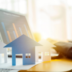 Paper cutouts of houses on a desk with laptop showing property investment charts, symbolizing Ohio real estate market analysis.
