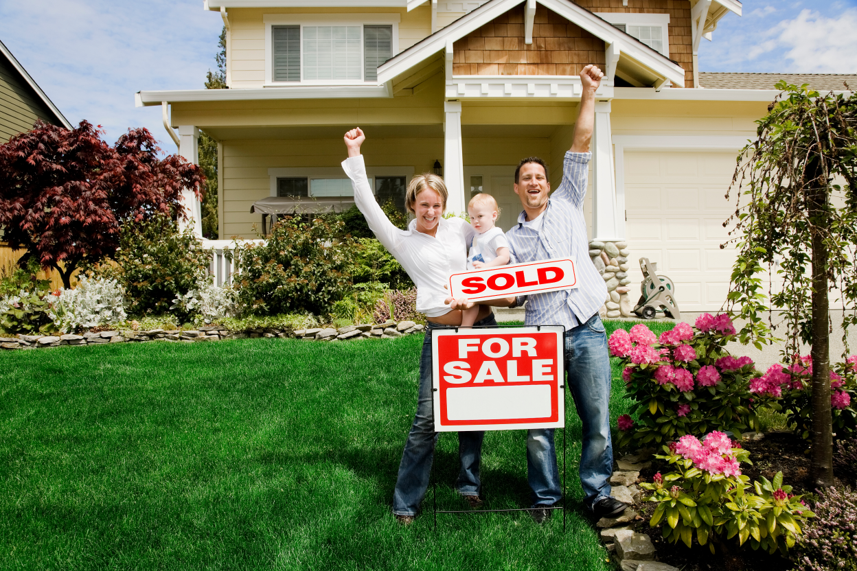Happy family celebrating with a 'SOLD' sign in front of their Cincinnati home, depicting a successful and quick sale by following expert real estate advice.