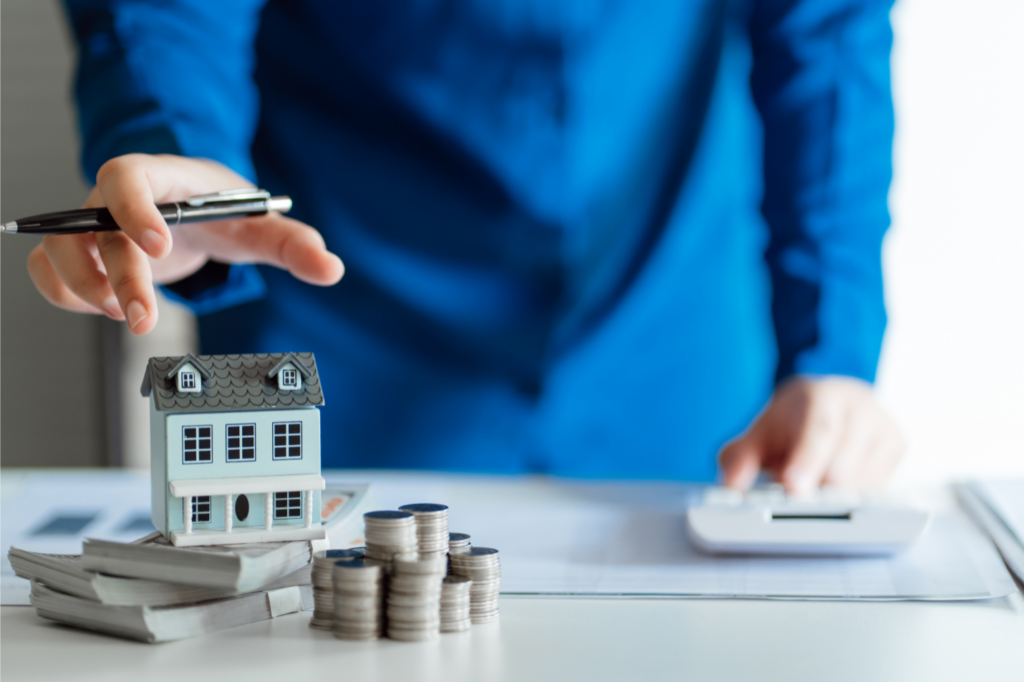 Real estate agent calculating costs with a model house and coins, depicting affordable selling in Toledo, Ohio.