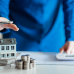Real estate agent calculating costs with a model house and coins, depicting affordable selling in Toledo, Ohio.