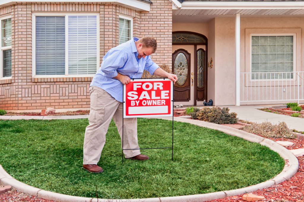 Homeowner placing a 'For Sale By Owner' sign on the front lawn of a Cincinnati suburb home