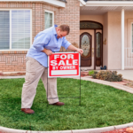 Homeowner placing a 'For Sale By Owner' sign on the front lawn of a Cincinnati suburb home