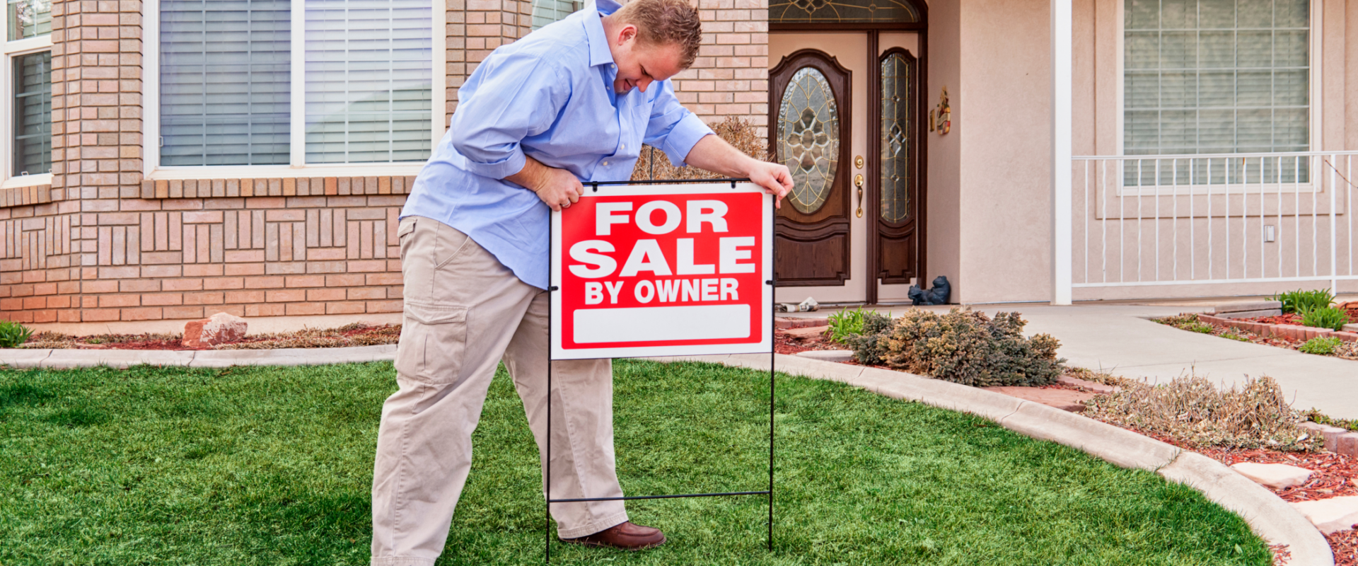 Homeowner placing a 'For Sale By Owner' sign on the front lawn of a Cincinnati suburb home