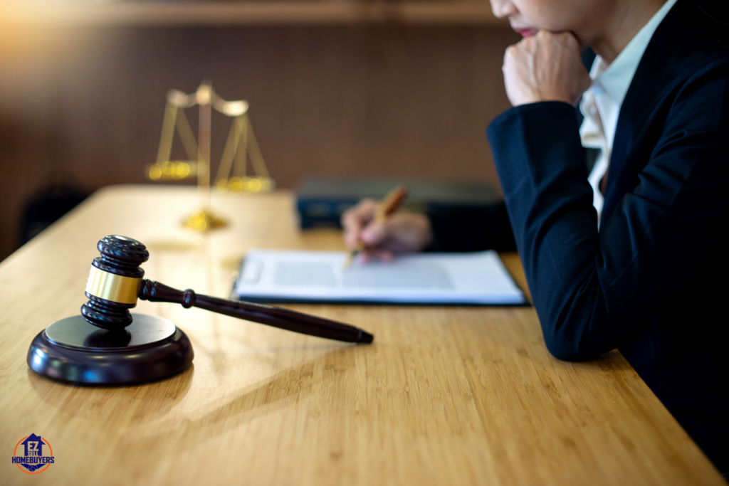 Close-up of a legal professional sitting at a wooden desk, reviewing documents with a pen in hand. A gavel and balance scale are in the background, symbolizing justice. The EZ Sell Homebuyers logo is visible, highlighting real estate legal issues in Ohio.