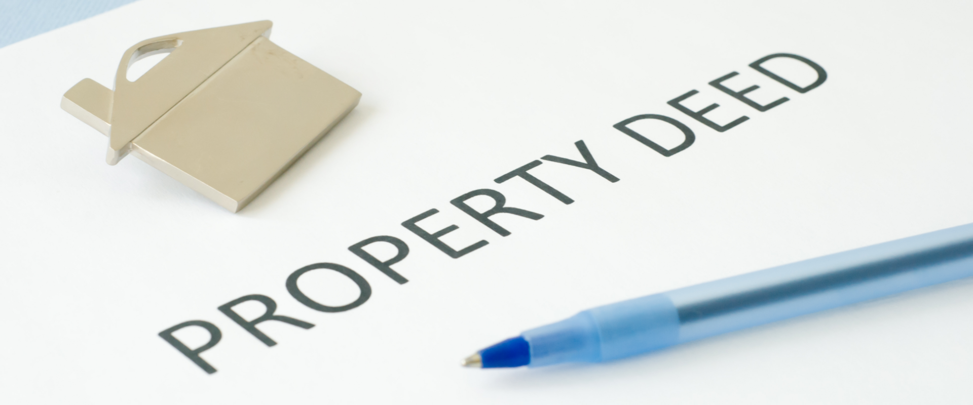 Property deed document with a house-shaped keychain and a pen, representing the process of removing a person's name from a deed in Ohio.