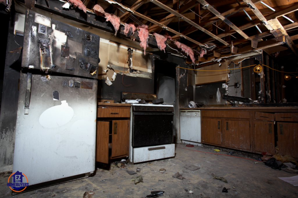 Fire-damaged kitchen in a Cincinnati home showing charred appliances, exposed ceiling beams, and extensive smoke damage, illustrating the challenges of selling a fire-damaged property.