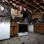 Fire-damaged kitchen in a Cincinnati home showing charred appliances, exposed ceiling beams, and extensive smoke damage, illustrating the challenges of selling a fire-damaged property.