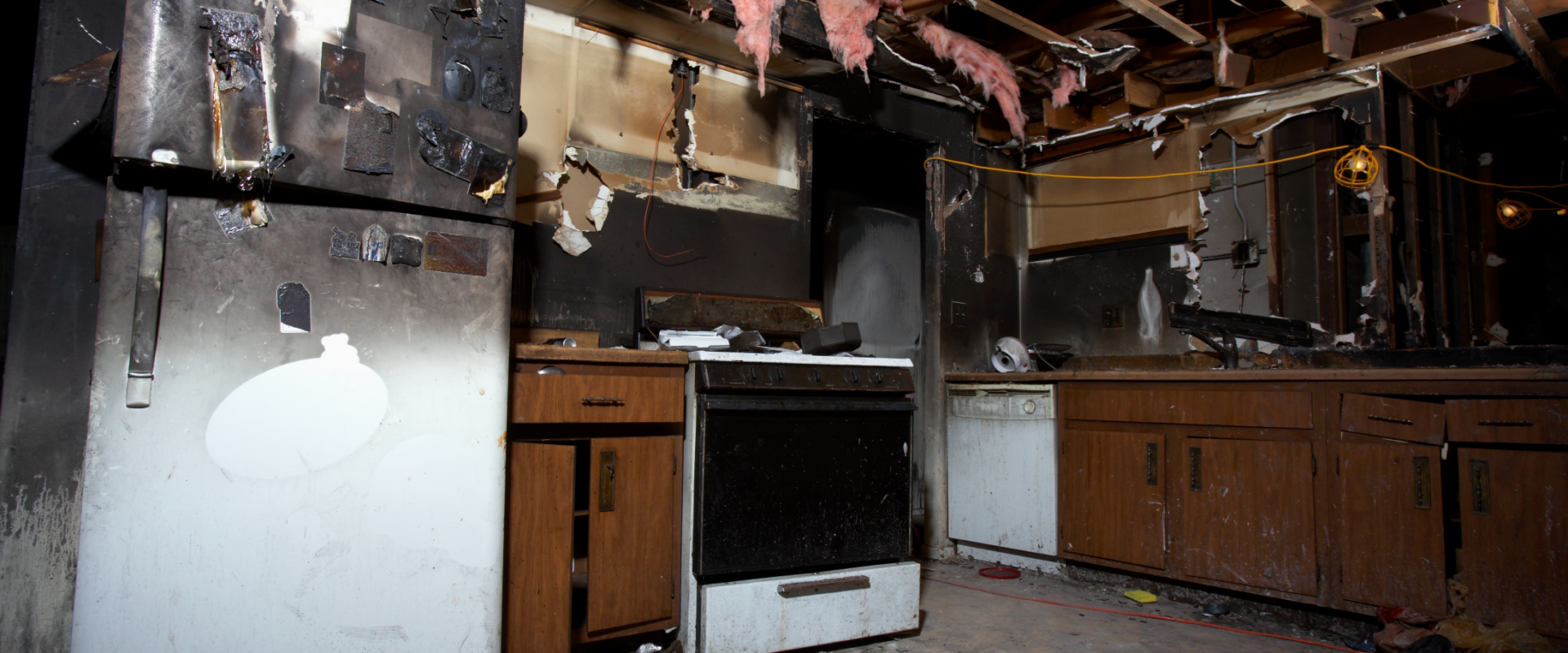 Fire-damaged kitchen in a Cincinnati home showing charred appliances, exposed ceiling beams, and extensive smoke damage, illustrating the challenges of selling a fire-damaged property.