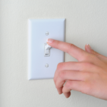 Close-up of a hand turning off a light switch, representing the legal complexities of utility shutoffs for squatters in Ohio as discussed in the article on handling squatter utility management and eviction processes.