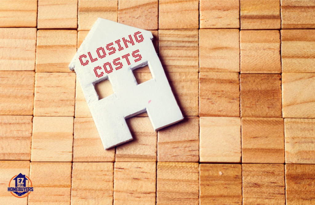 Image of a wooden block surface with a white house-shaped cutout labeled 'Closing Costs,' representing the concept of real estate closing costs in Ohio. EZ Sell Homebuyers logo in the corner.