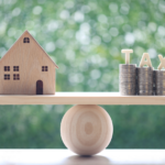 Wooden house model balanced with stacked coins labeled 'TAX' representing strategies to lower property taxes in Ohio, illustrating savings methods such as appeals and exemptions.