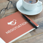 Notebook with the word 'Negotiation' on the cover, pen, eyeglasses, and coffee cup on a wooden table, symbolizing strategies for handling offer negotiations when selling a house in Ohio.