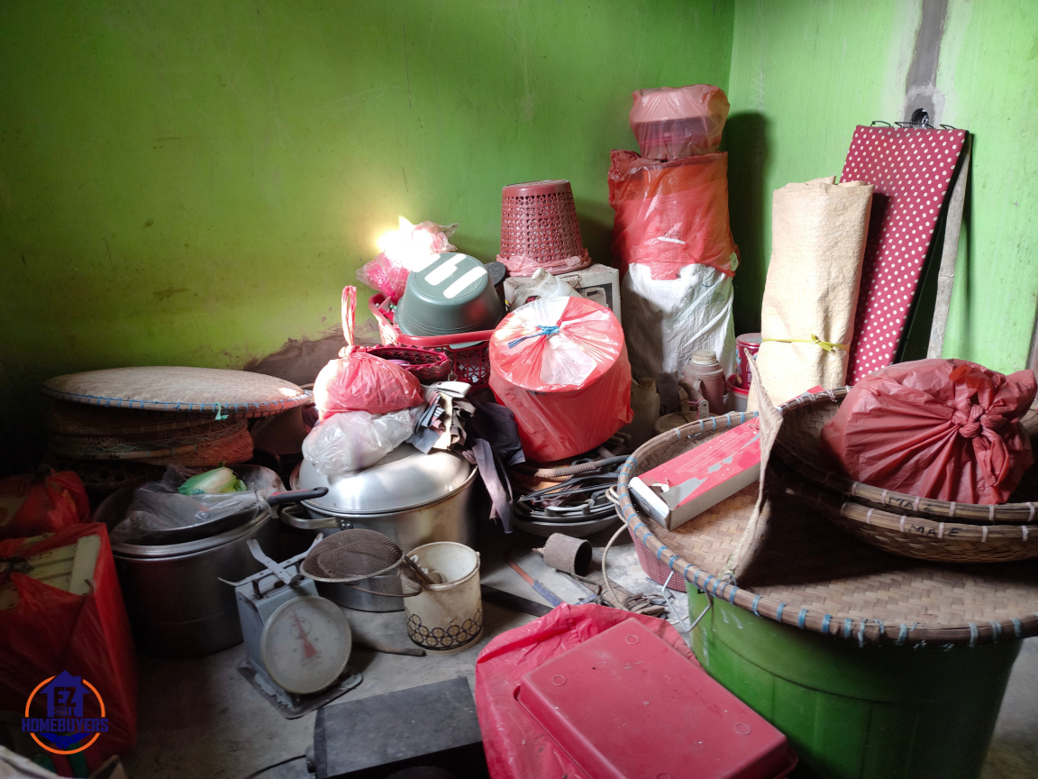 Cluttered room with various household items and red plastic bags in a hoarded house. The image illustrates hoarding conditions that could lead to a house being condemned in Ohio due to safety and health hazards. Items piled up against green-painted walls, creating potential fire risks and blocked pathways.