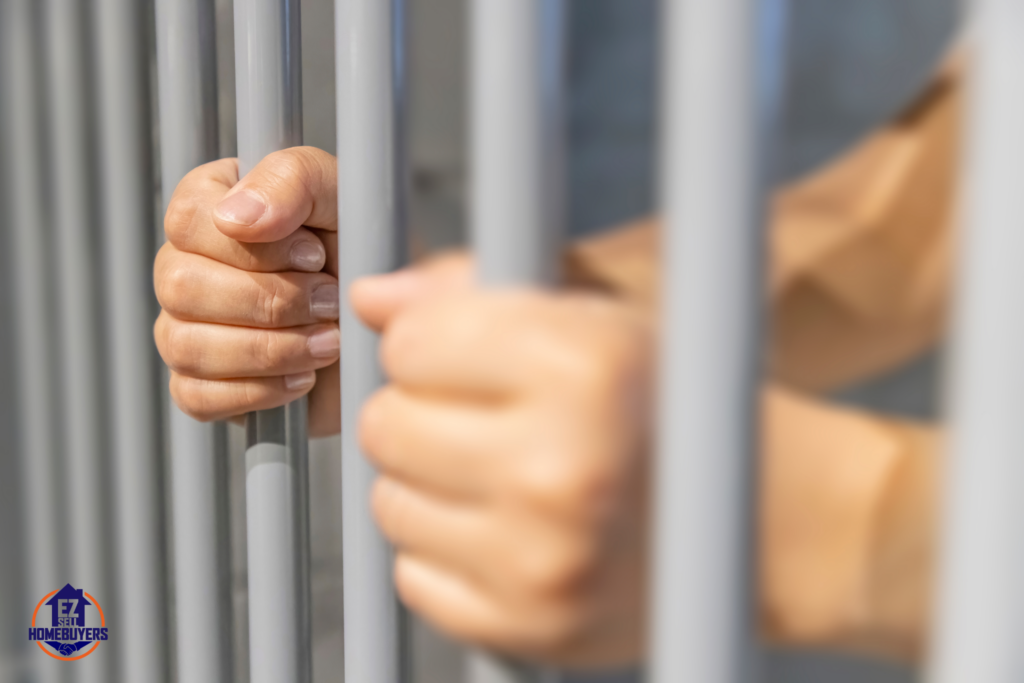 Hands gripping jail bars representing challenges of selling a house in Ohio with an incarcerated spouse, with the EZ Sell Homebuyers logo indicating fast cash sale solutions.