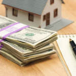 Stacks of cash with a model house and notebook symbolizing the benefits of selling a house for cash in Ohio, highlighting the faster sale process and fewer fees.