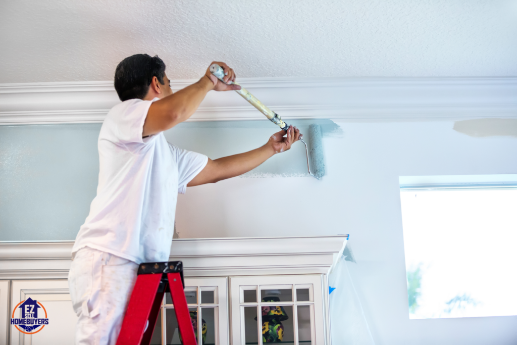 DIY home painting project in Ohio – A professional painter using a roller to apply light blue paint on an interior wall near crown molding. Budget-friendly home improvement idea.
