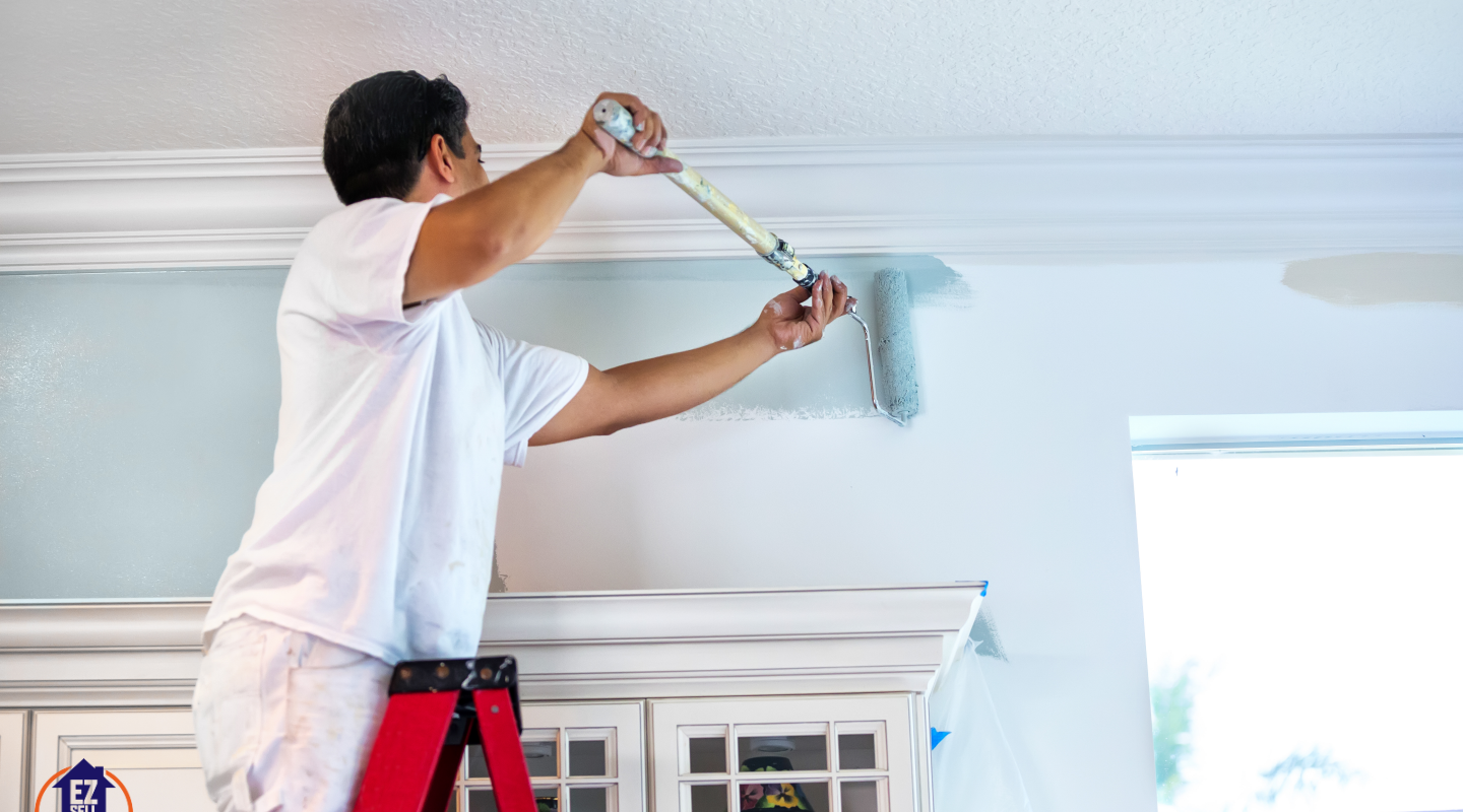 DIY home painting project in Ohio – A professional painter using a roller to apply light blue paint on an interior wall near crown molding. Budget-friendly home improvement idea.