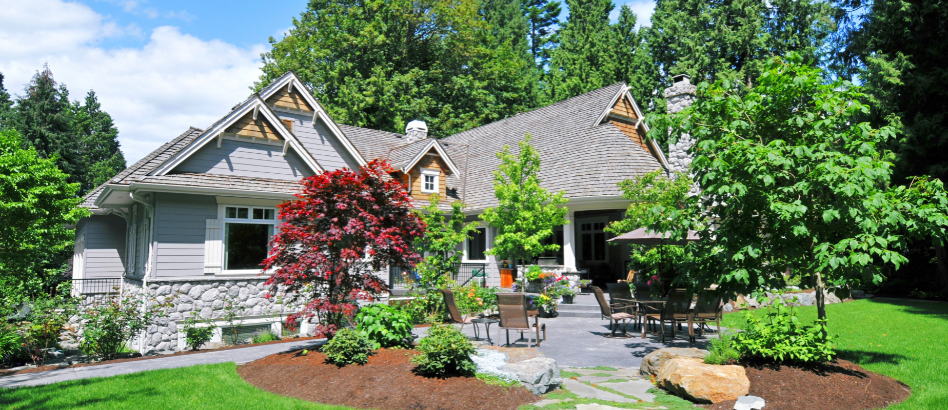 Beautifully landscaped Ohio home with lush green lawn, trimmed bushes, vibrant spring flowers, and an inviting outdoor patio—boosting curb appeal for a fast home sale. EZ Sell Homebuyers logo in the corner.