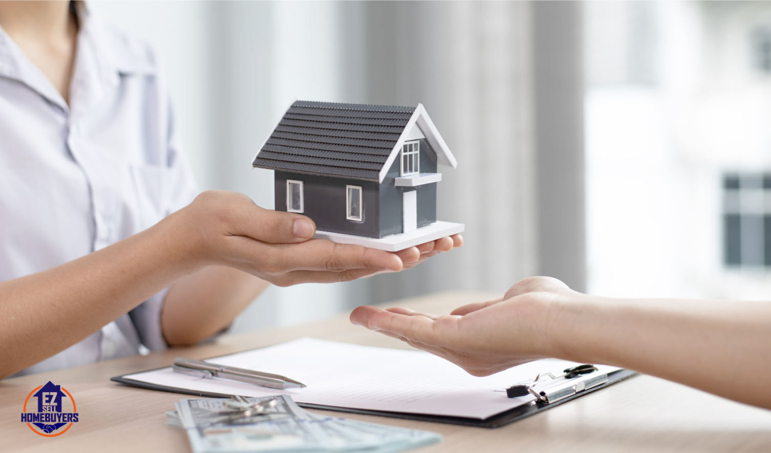 A person handing over a model house during a real estate transaction with contract paperwork and cash visible.
