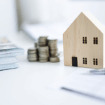 Mini wooden house model beside stacked coins symbolizing real estate investment growth and home value in Dayton, Ohio
