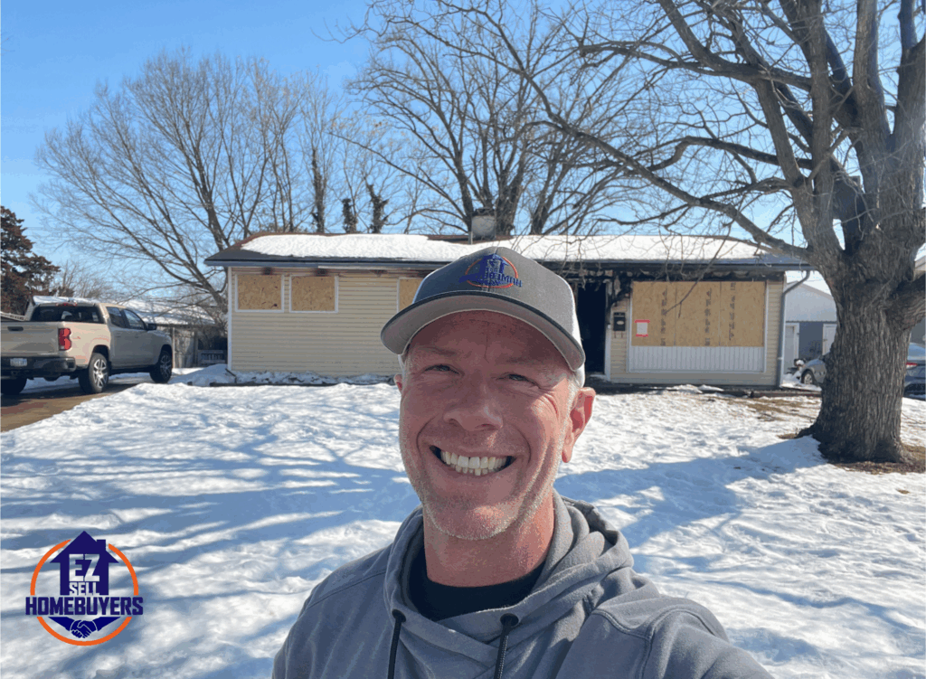 Mike Wall of EZ Sell Homebuyers standing in front of a boarded-up fire-damaged house in Dayton, Ohio, offering to buy homes as-is for cash.