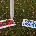 For sale sign riders - price reduced rider and open house rider in front of a Massachusetts single-family home in the fall