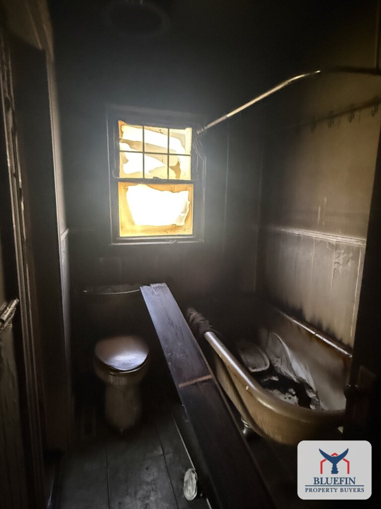 Bathroom coated in black soot after a house fire in Massachusetts, with a clawfoot tub and heat-damaged window
