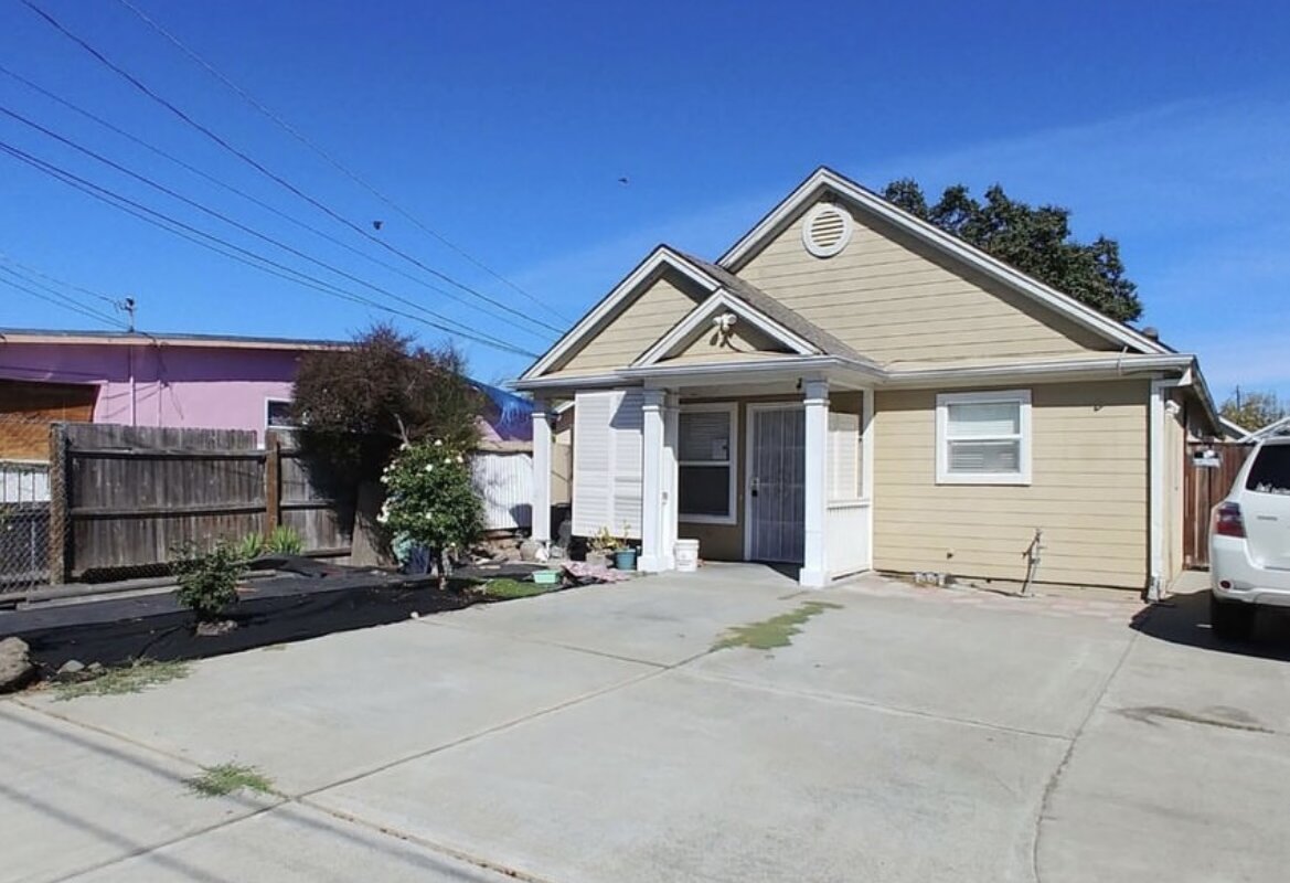 Single-story tan house with white trim and text overlay reading “Facing Foreclosure?” under a clear blue sky.