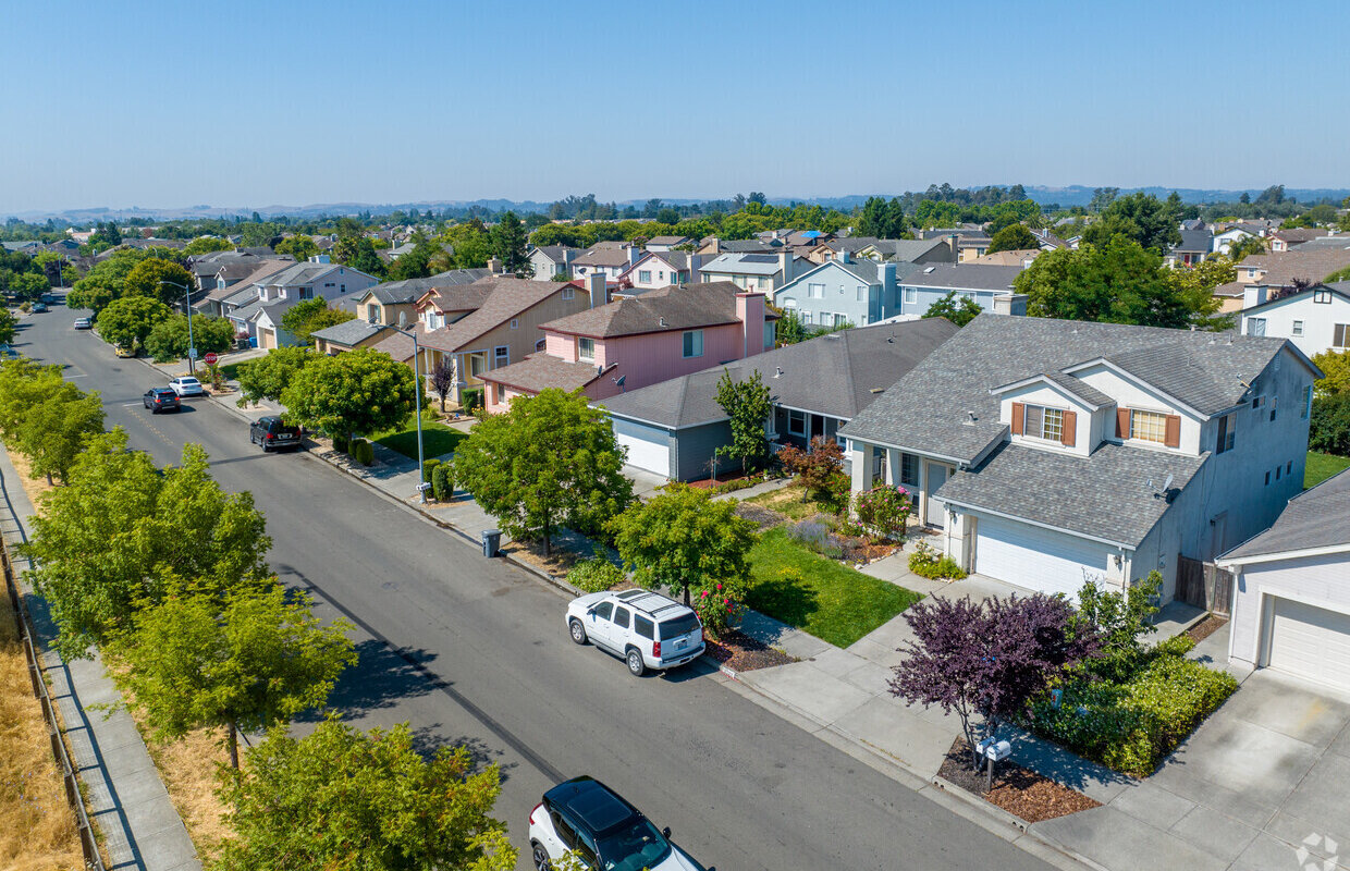 Aerial view of a quiet suburban neighborhood with tree-lined streets and modern two-story homes on a clear day.