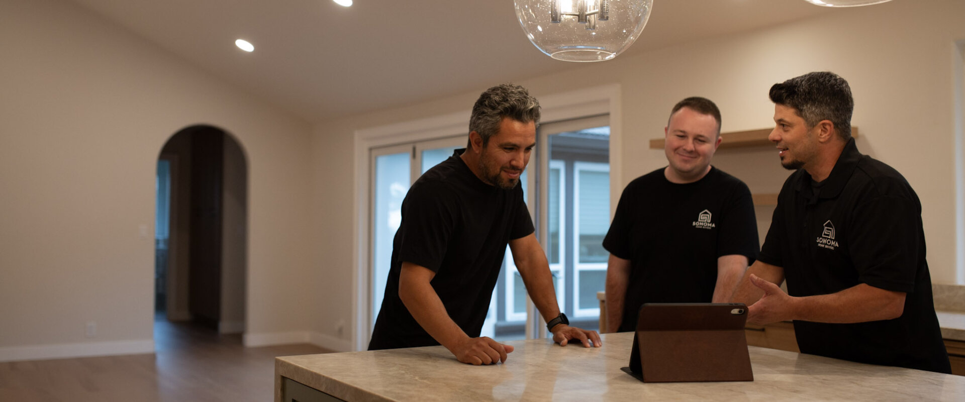 Brian and Wyatt from Sonoma Home Buyers meeting with a client at a kitchen island, reviewing options on a tablet in a Sonoma County home.