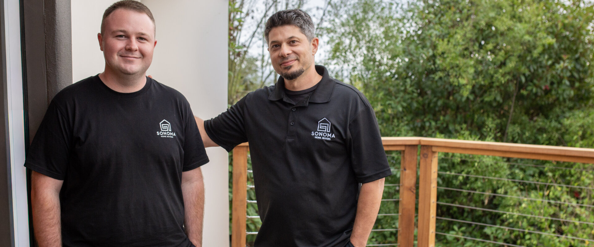 Brian Kraut and Wyatt Postal of Sonoma Home Buyers on a residential deck in Sonoma County, wearing branded shirts with trees in the background.