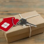 Keychain house and keys in gift box on wooden background. Real estate